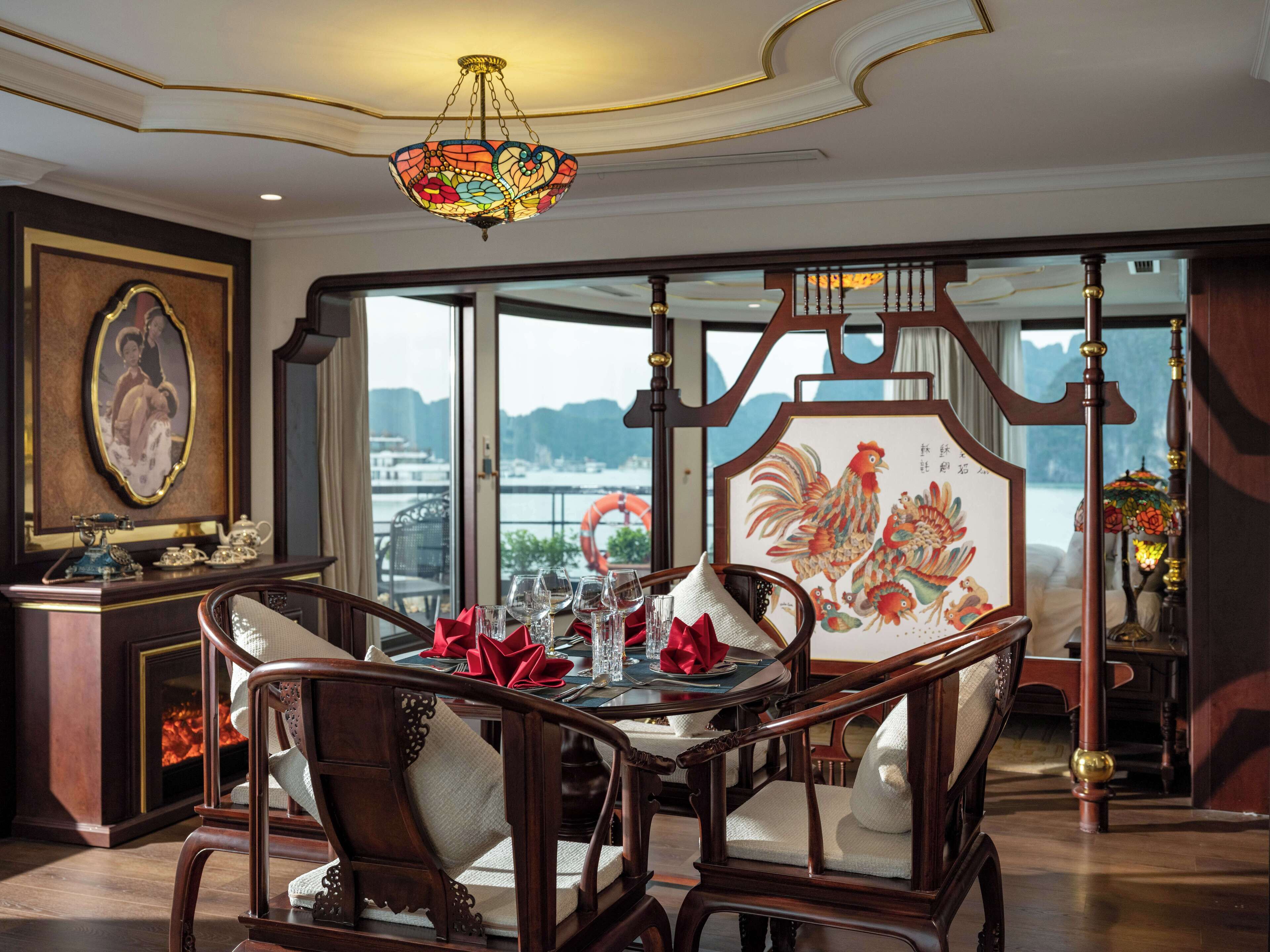 Un coin repas avec vue sur une rivière, une table dressée dans un style traditionnel avec des serviettes rouges et un luminaire décoratif au plafond.
