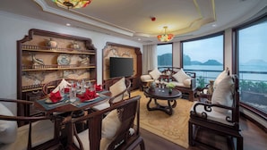 A traditional-style living room with a dining area, large windows, and a view of the water. - L'amour Cruise (Tuan Chau)