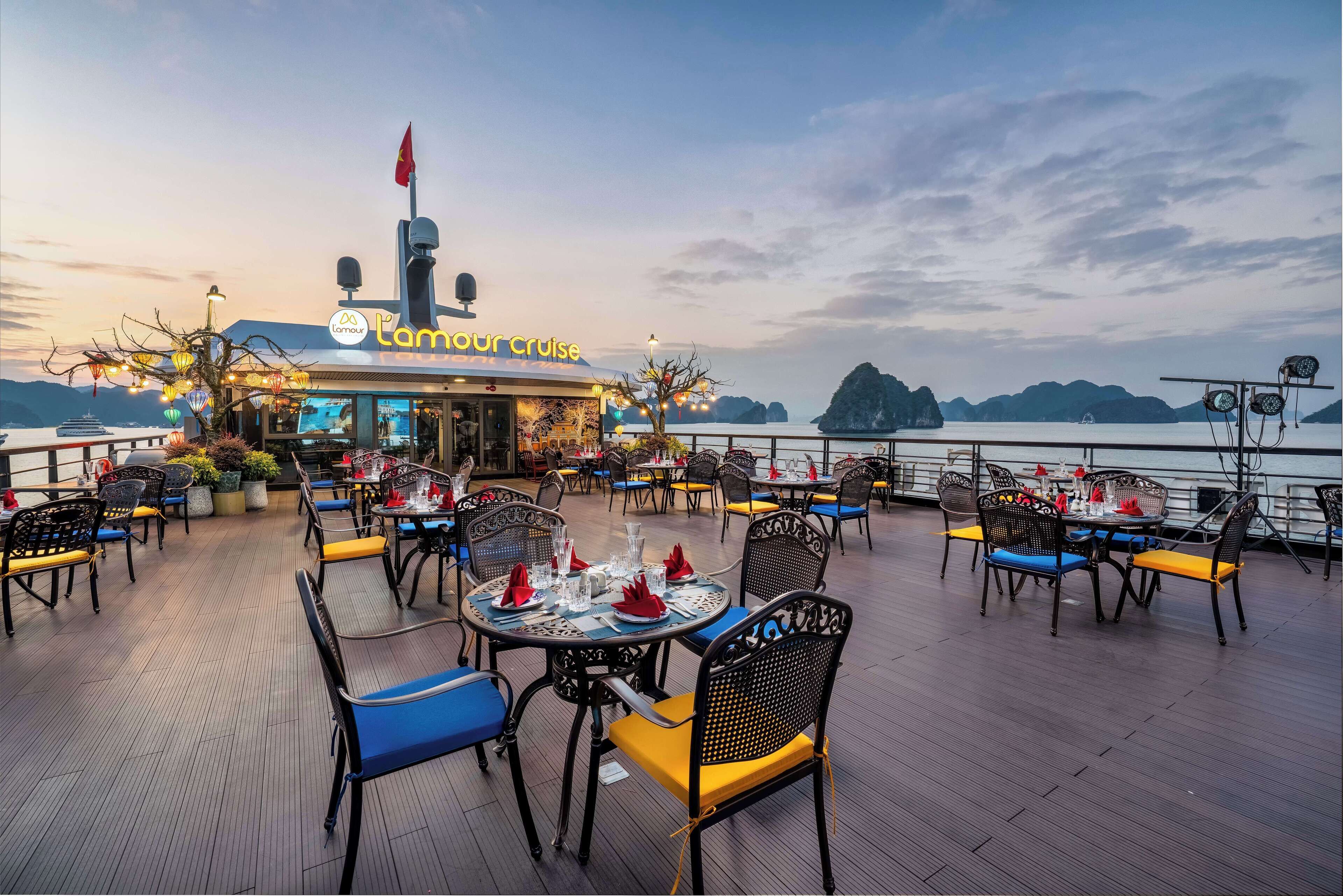 Un restaurante con terraza al aire libre, con vistas a un cuerpo de agua y montañas distantes.