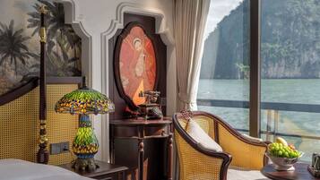 Une chambre d’hôtel avec un lit, une chaise, une table avec des fruits, une lampe décorative et un tableau.