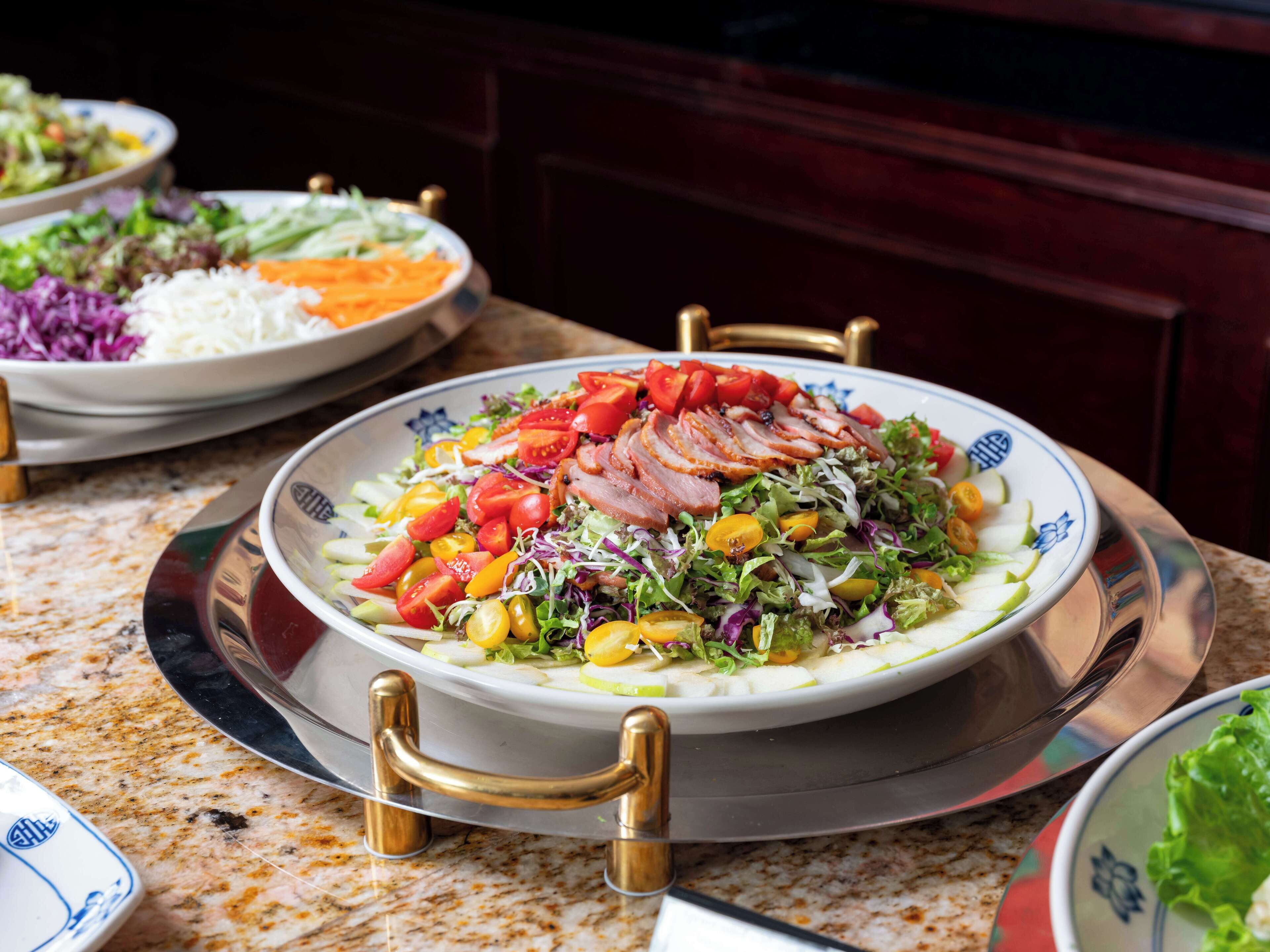 A dining table with a variety of dishes, including a salad with sliced meat and vegetables, and other plates with different food items.