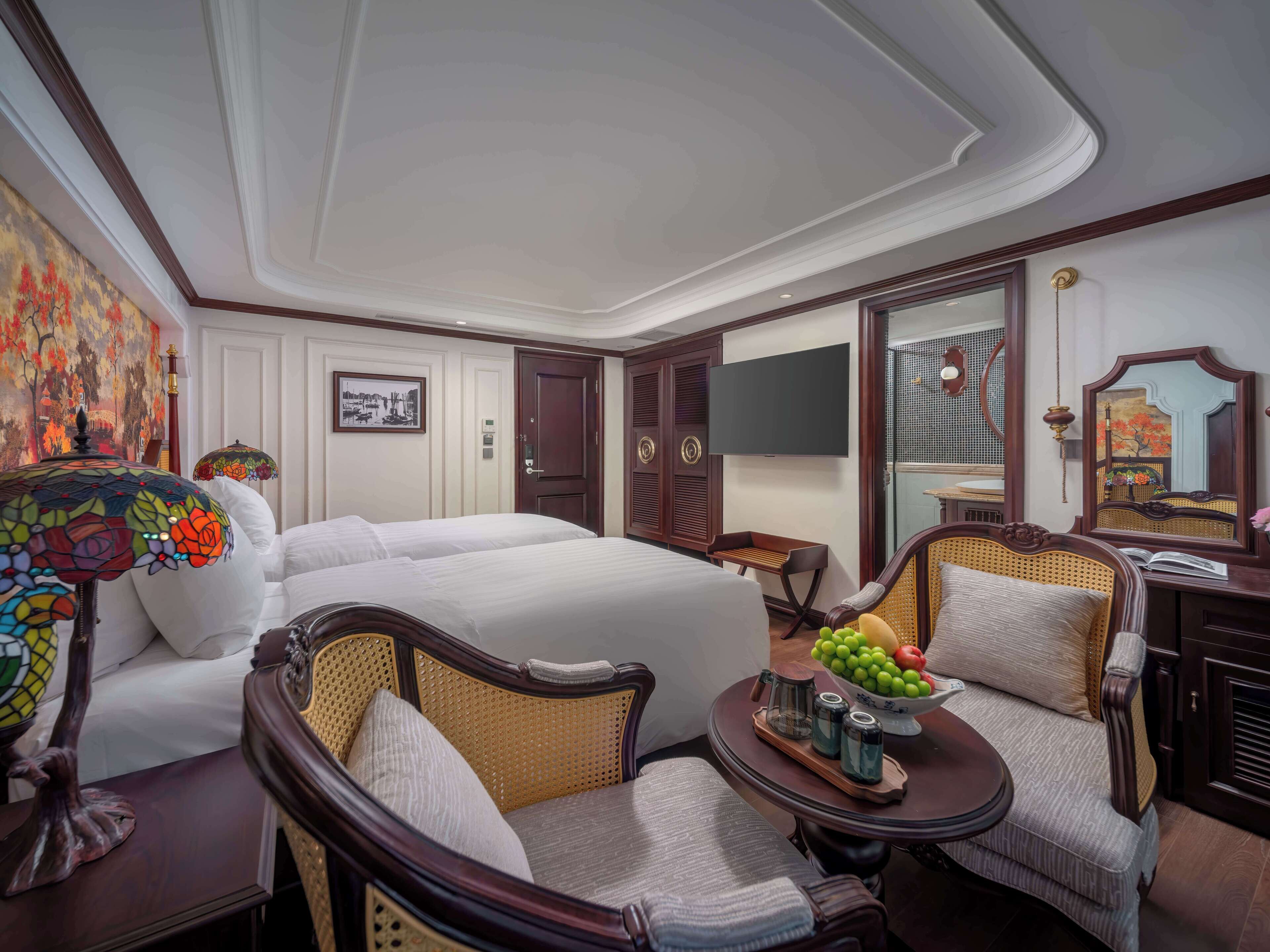 Hotelkamer met een groot bed, twee fauteuils, een tafeltje met een schaal fruit, een televisie en een spiegel.