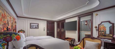 Hotelkamer met een groot bed, twee fauteuils, een tafeltje met een schaal fruit, een televisie en een spiegel.