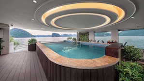 A pool area with a wooden deck, a built-in bar, and a view of the water. - L'amour Cruise (Tuan Chau)