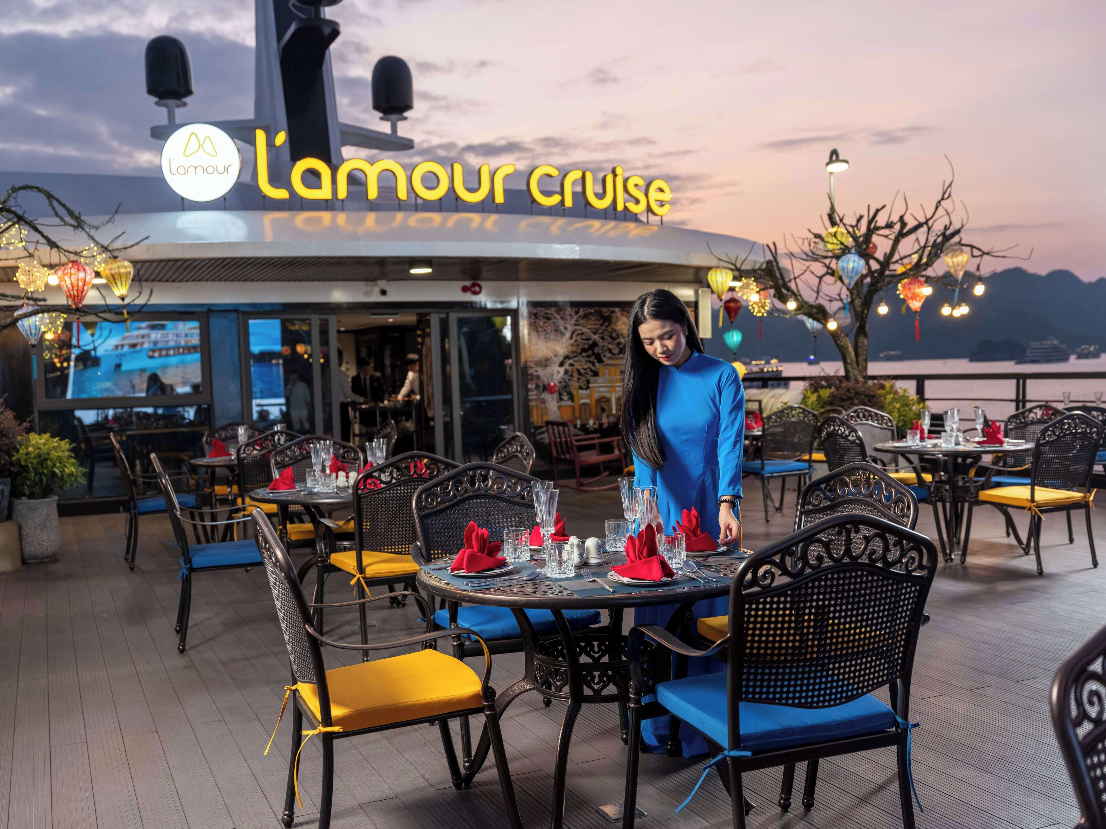 Un restaurant doté d’une terrasse, de tables dressées avec des serviettes et des verres rouges, et offrant une vue sur la mer.