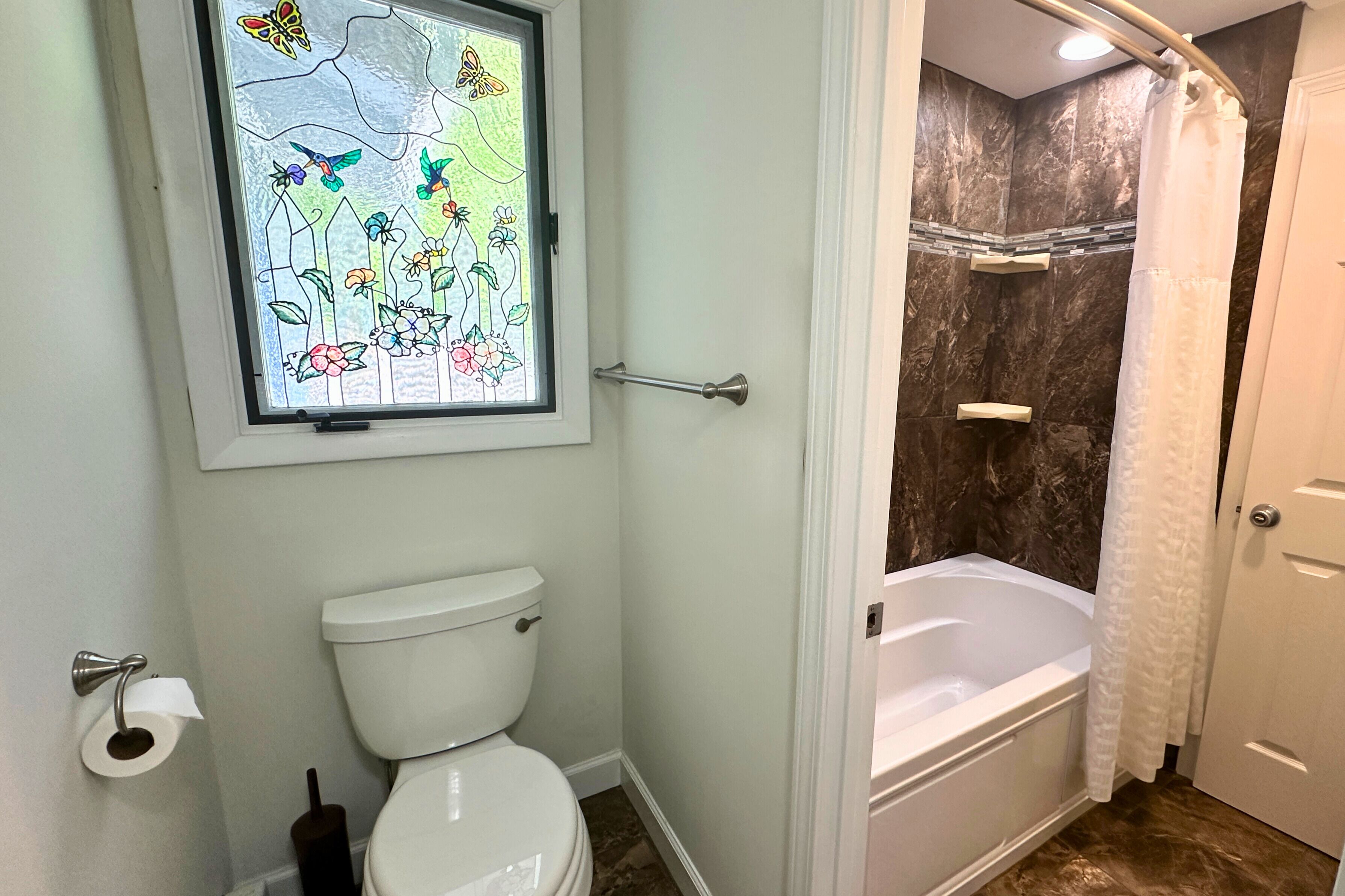 A bathroom with a toilet, a shower, a bathtub, and a stained glass window above the toilet.