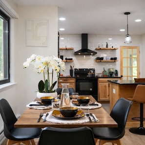 A modern dining area with a wooden table set for four, surrounded by black chairs. A vase with white flowers is placed on the table.