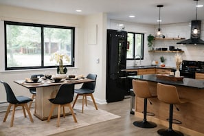 A modern kitchen with a central island, black appliances, and a dining area with chairs and a table set for a meal.