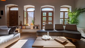 A modern living room with a sofa, a coffee table, and a bench. There are three arched windows providing natural light.