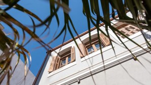 A building with a white facade, wooden shutters on windows, and a clear blue sky in the background.