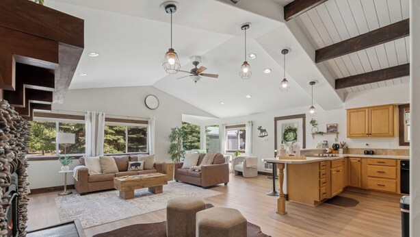 A spacious living area with a high ceiling, wooden beams, and a large window offering a view of greenery. - Spacious 7-Bed Home w/ Hot Tub, Fireplace, Gym, Wine Bar, and 2 Living Spaces! (Lakeside)