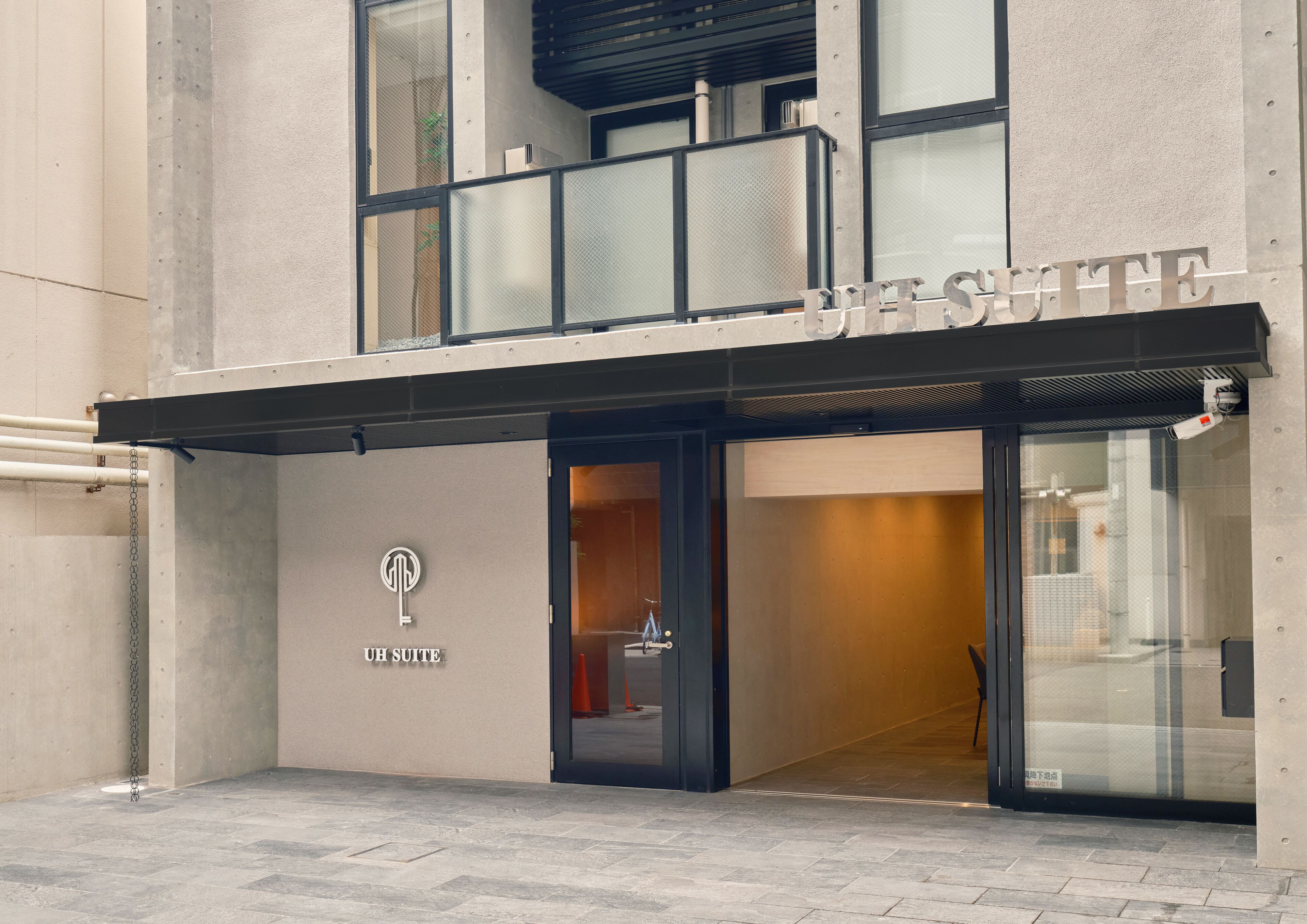 A modern hotel entrance with a glass facade, a metal awning, and a visible sign reading "JESS SUTTE."