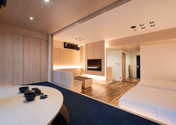 A modern hotel room with a wooden floor, a bed, a desk with a flat-screen TV, and a seating area with a table and chairs. - UH SUITE NAMBA STATION (Osaka)