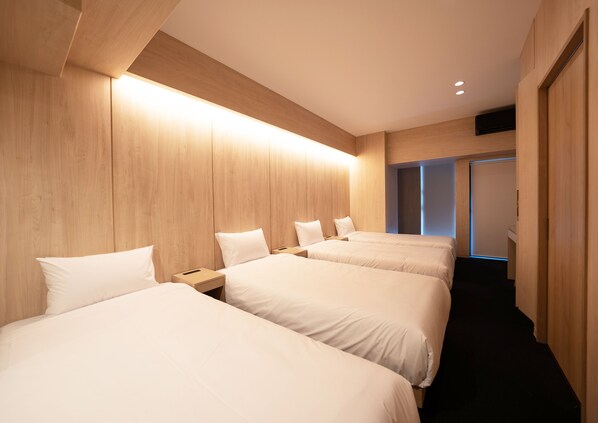 Une chambre d’hôtel avec trois lits, des lambris en bois et un couloir menant à une porte.