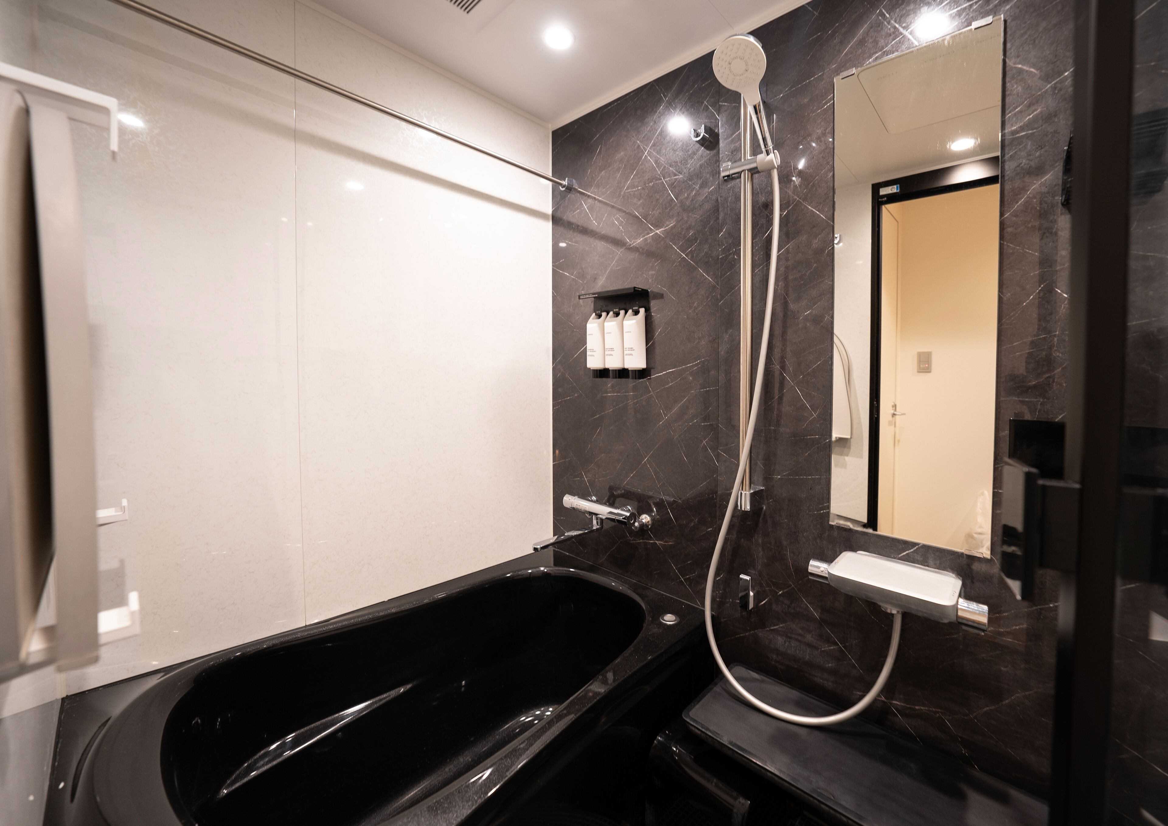 Un baño moderno con una bañera negra, un cabezal de ducha de mano y un espejo grande.