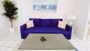 Une pièce avec un canapé bleu, une petite table basse, une plante en pot et un tableau représentant des voiliers accroché au mur.