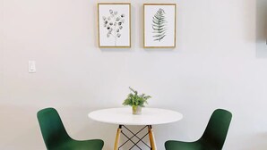 A round table with a white top and two green chairs with black legs. Above the table, there are two framed botanical prints on the wall. - Comfortable SoBe Studio | Balcony | Free Beach Chairs & More (Miami Beach)