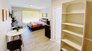 A compact room with a bed, a small desk, a chair, and a shelving unit. - Comfortable SoBe Studio | Balcony | Free Beach Chairs & More (Miami Beach)
