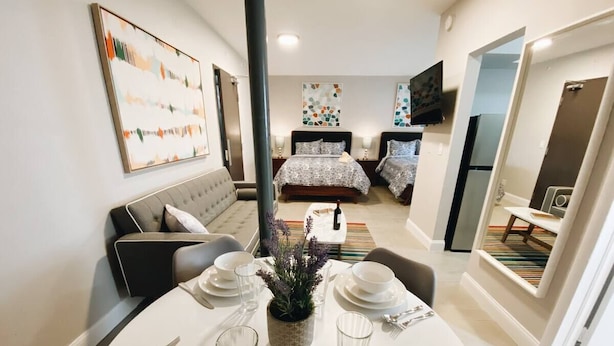 A dining area with a table set for four, a sofa, and a bed in the background.