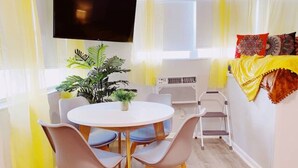 A room with a round table, four chairs, a potted plant, a flat-screen TV, an air conditioning unit, and a bed with a yellow blanket. - Accessible South Beach Unit w/ Free Perks (Miami Beach)