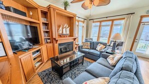 A spacious living room with a large TV, wooden shelving, a fireplace, and a sofa set. - Accessible Semi-Soundfront: Pool, Hot Tub, Game Rm, Elevator, Boat Ramp, Linens (Rodanthe)