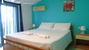A neatly made bed with white linens and towels, a wooden headboard, a wall-mounted air conditioner, and a nightstand with a lamp. - Green Bay B16 - Three-room apartment on the 2ndFloor (Pineto)