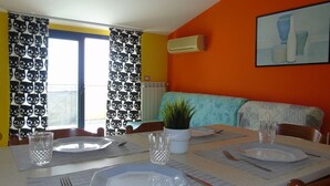 A dining area with a table set for four, a potted plant, and a sofa in the background. - Green Bay B16 - Three-room apartment on the 2ndFloor (Pineto)