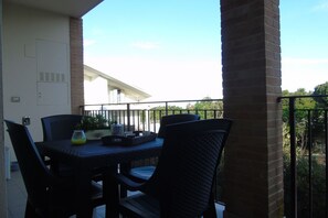A balcony with a table and chairs, a potted plant, and a view of a building in the background.