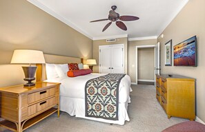 Habitación de hotel con cama, lámparas de noche, ventilador de techo, armario y un cuadro en la pared.