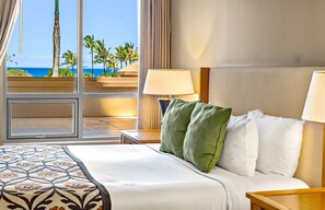 A hotel room with a bed, two bedside lamps, a view of the ocean, and a window with curtains.