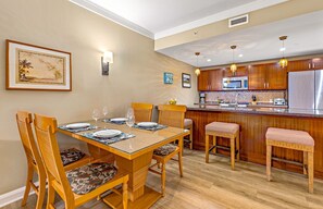 A dining area with a wooden table set for four, surrounded by wicker chairs with cushioned seats.