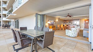 Een modern appartement met een glazen eettafel, rieten stoelen, een keuken met houten kasten en een balkon met uitzicht op de gevel.