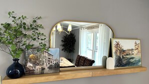 Een spiegel met een houten plankje, een vaas met groene planten en twee ingelijste foto's.