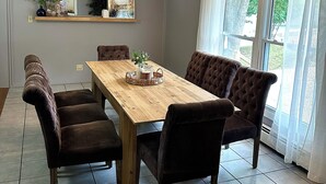 Een eetkamer met een houten tafel, zes gestoffeerde stoelen, een kroonluchter, een spiegel en een raam met gordijnen.