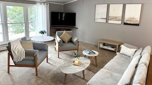 Een woonkamer met een grijze bank, fauteuils, een salontafel en een aan de muur bevestigde televisie.