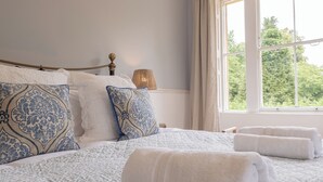 A neatly made bed with patterned pillows, a bedside lamp, and a view of greenery through a window. - Gorgeous 3BD in Oxfordshire Countryside (Bicester)