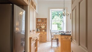 A kitchen with wooden cabinets, a stainless steel refrigerator, a dining table with chairs, and a window with a view of greenery. - Gorgeous 3BD in Oxfordshire Countryside (Bicester)