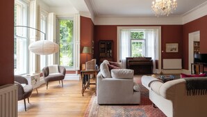 A spacious living room with a large chandelier, a piano, and a television. - Gorgeous 3BD in Oxfordshire Countryside (Bicester)