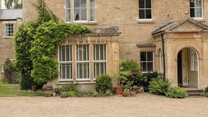 A large stone building with multiple windows, a central entrance with a pediment, and a gravel driveway. - Gorgeous 3BD in Oxfordshire Countryside (Bicester)