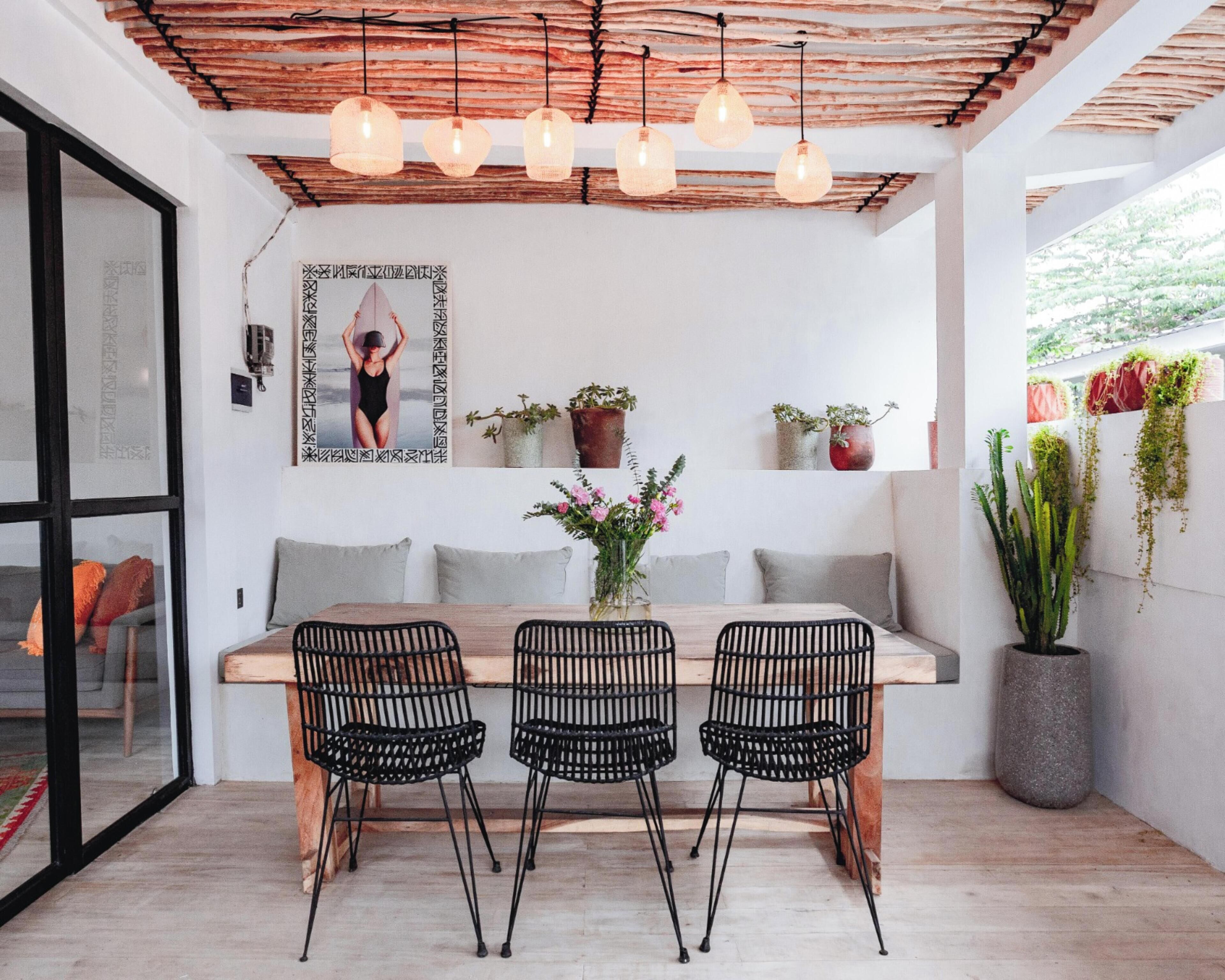 A modern dining area with a wooden table and black chairs, a ceiling with exposed beams, and potted plants on the walls.