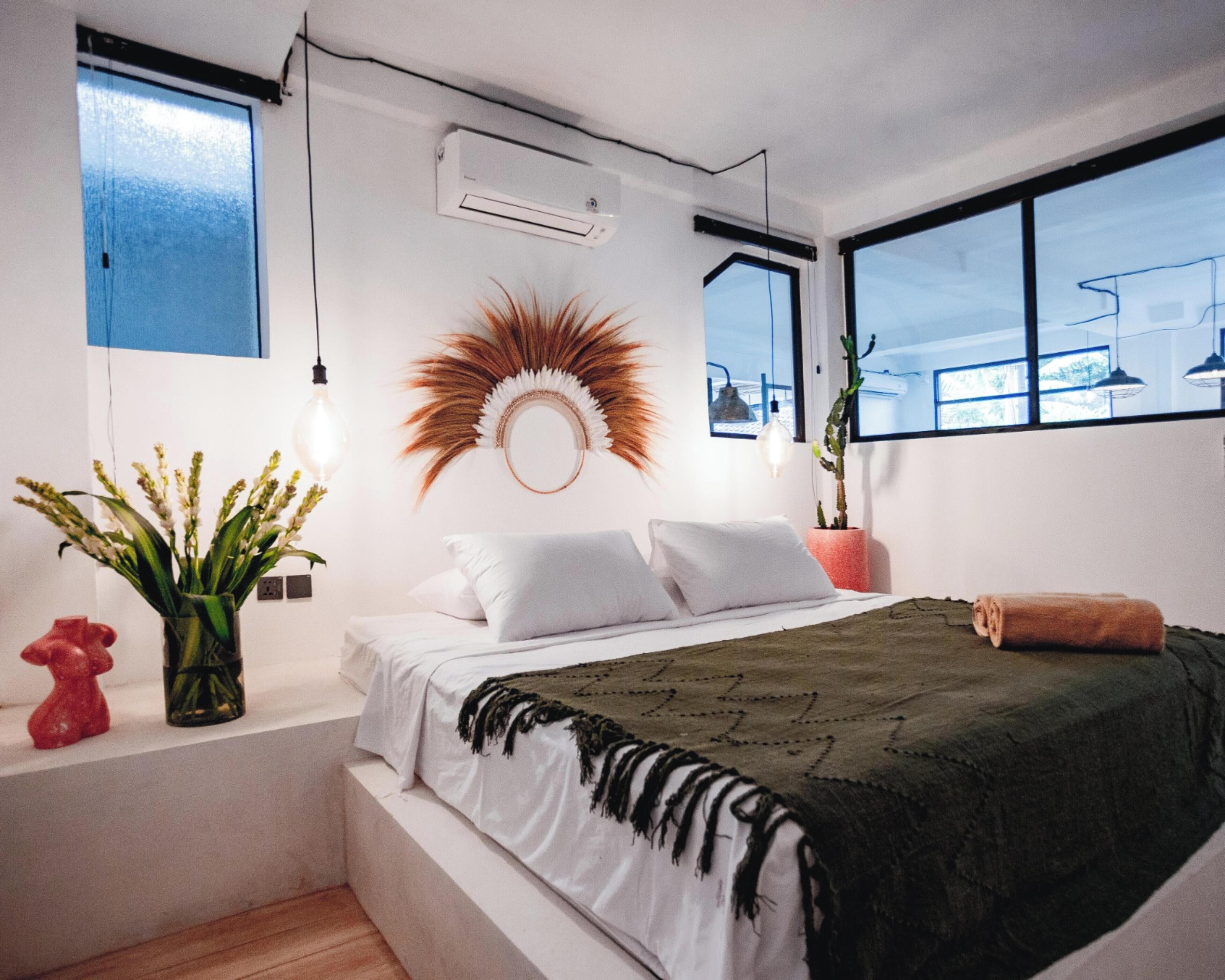 Ein modernes Schlafzimmer mit einem Bett, einem dekorativen Spiegel, einer Topfpflanze und einem Fenster mit Aussicht.