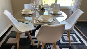 A dining table set with white chairs, plates, and glassware. - Entire Home in Edmonton South close to Airport with fenced private yard & deck (Edmonton)