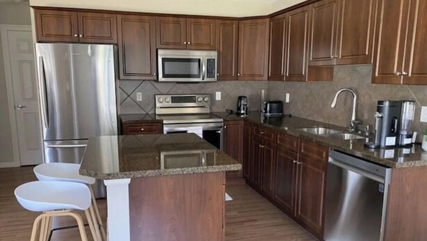 A modern kitchen with wooden cabinets, stainless steel appliances, and a granite countertop. - Entire Home in Edmonton South close to Airport with fenced private yard & deck (Edmonton)