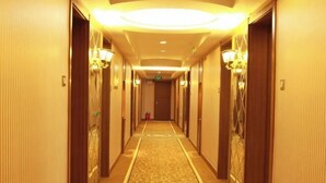 A hotel hallway with a carpeted floor, wooden doors, and wall-mounted lamps. - Wolff Hotel (Suifenhe)