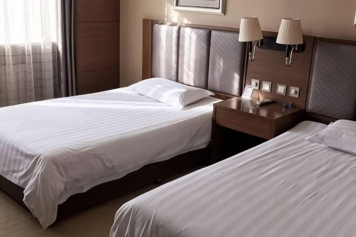A hotel room with two beds, a nightstand, lamps, and a framed picture on the wall.