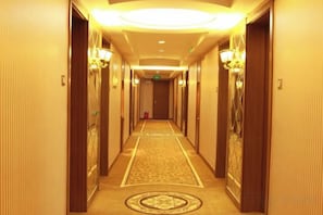 A hotel hallway with carpeted floors, wooden doors, and wall-mounted light fixtures. - Wolff Hotel (Suifenhe)