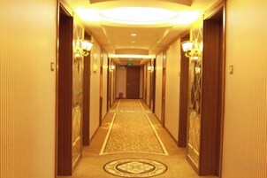 Un pasillo de hotel con pisos alfombrados, puertas de madera y luminarias fijadas a la pared.