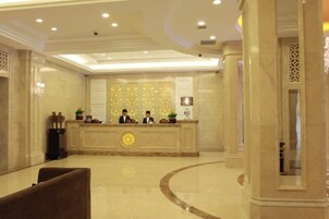 Zona de recepción de un hotel con mostrador de mármol, tres recepcionistas y un diseño de techo moderno.