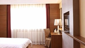 A hotel room with a bed, a desk with a lamp, a chair, and a large window with curtains. - Wolff Hotel (Suifenhe)