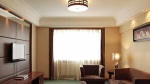 A hotel room with a large window, a flat-screen TV mounted on the wall, a sofa, a small table, and a lamp. - Wolff Hotel (Suifenhe)